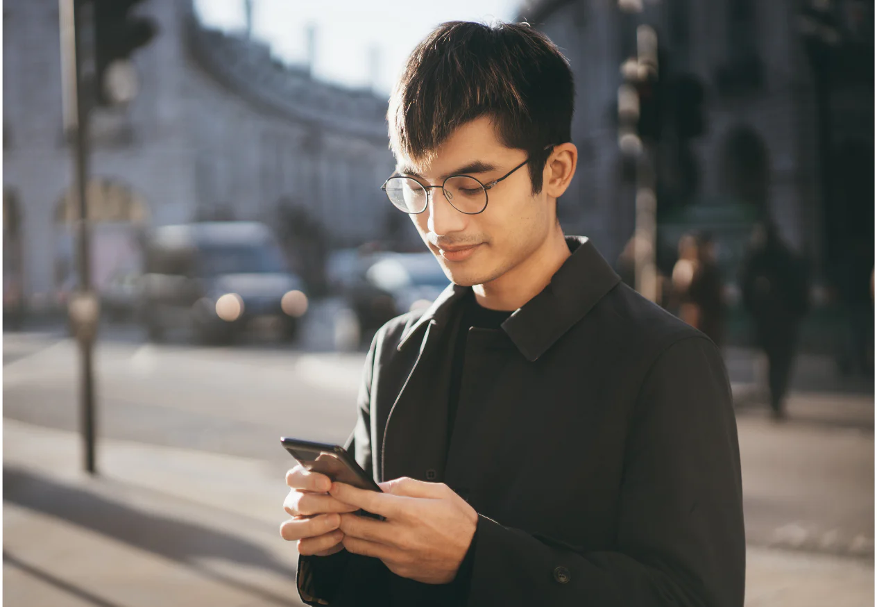 Young Man Using Smartphone on City Street Man with glasses using smartphone on a city street in daylight